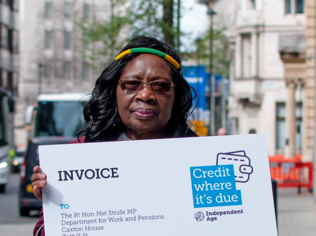Older woman holding invoice placard that says 'Credit where it's due: Pension credit invoice to the Department of Work and Pensions'