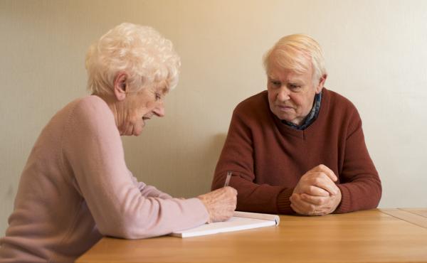 An older couple sit at a table talking and making notes