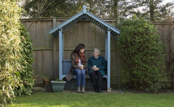 A woman and an older woman sit talking in the garden