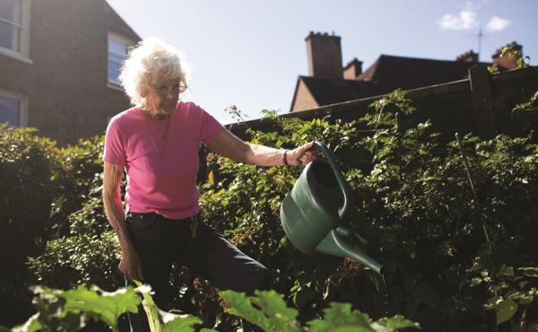 An older woman waters the garden