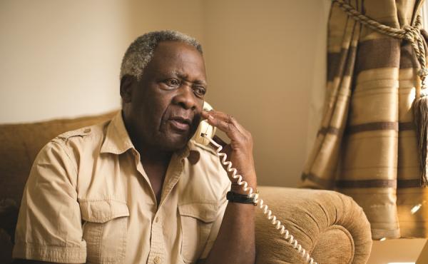 An older man sits in an armchair making a phone call
