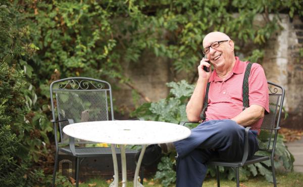 An older man on the phone smiling in his garden