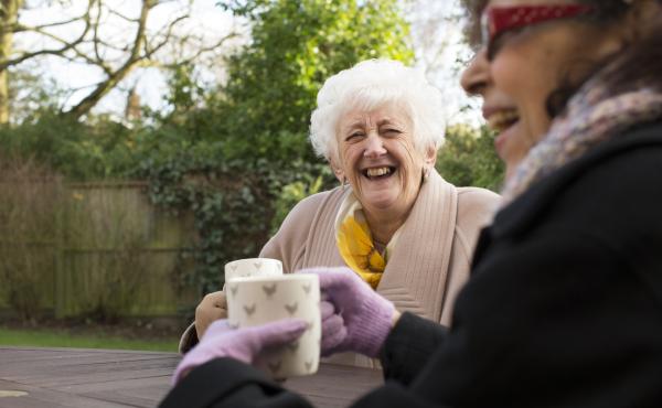 Two laughing older women drink tea in the garden