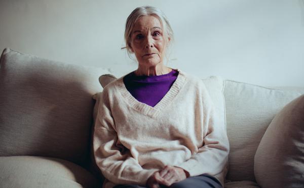 An older woman sitting on her sofa looking sad