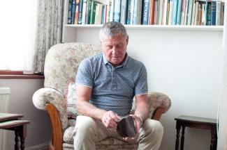 Older man sitting in armchair looks through his wallet