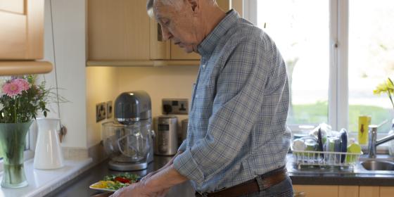 An older man chops vegetables in the kitchen