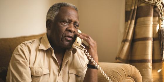 An older man sits in an armchair making a phone call
