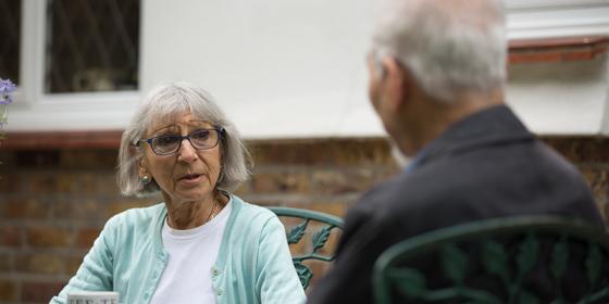 Woman with glasses and silver bobbed hair speaks to an older man in a garden
