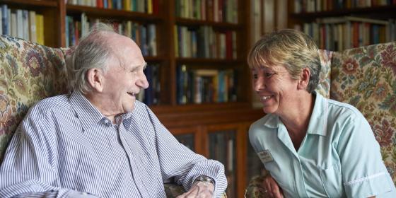 Older man and paid carer talking in care home