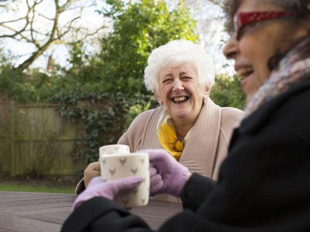 Two laughing older women drink tea in the garden