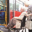 Older woman pushing man in wheelchair onto bus