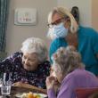 Care home worker wearing face mask talking to two women having a meal