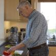 An older man chops vegetables in the kitchen