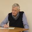 An older man sits at a table making notes