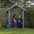 A woman and an older womn sit talking in the garden